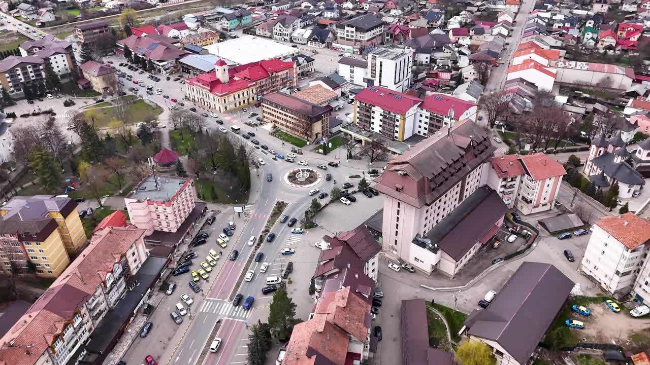 Luftfoto med drone av Gura Humorului sentrum som viser en travel rundkjøring med påskelysdekorasjoner, trafikk, bygninger og bystruktur i Romania.