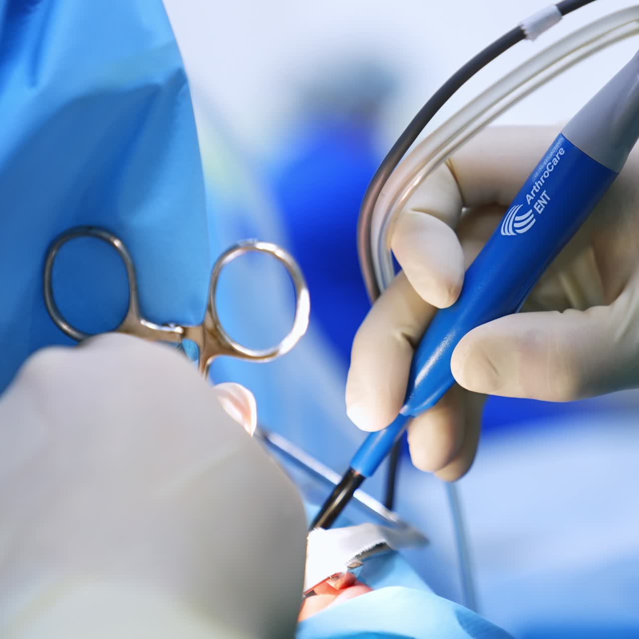 Gloved surgeon's hands hold the metal tool and electric device. Close up. Doctor slowly moves the medical appliance performing surgery. Blurred backdrop