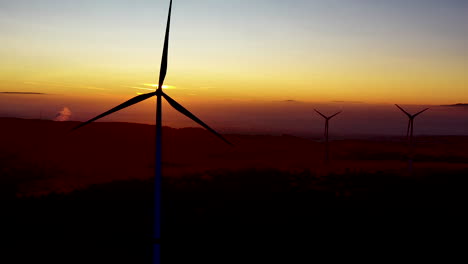 silhouettes of wind turbines spinning in front of scenic sunset sunlight, aerial view