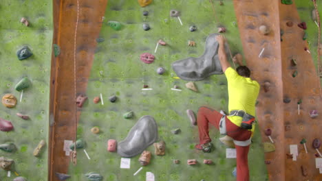 climber moves on the mountain in a room with a rope on the insurance and a bag for chalk overcoming the height rises to the top in slow motion.