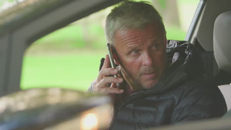 mature man sitting in car after accident making call on mobile phone with flashing police lights