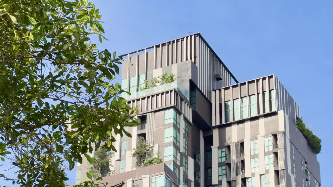 Contemporary hotel exterior with lush trees, clear daylight, slight upward camera movement, urban Bangkok setting