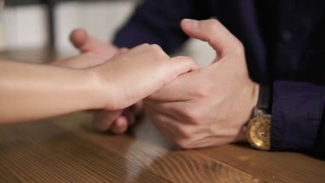 Close-Up-view-of-young-couple-holding-hands-sitting-at-the-wooden-table.-Romantic-date-of-loving-couple