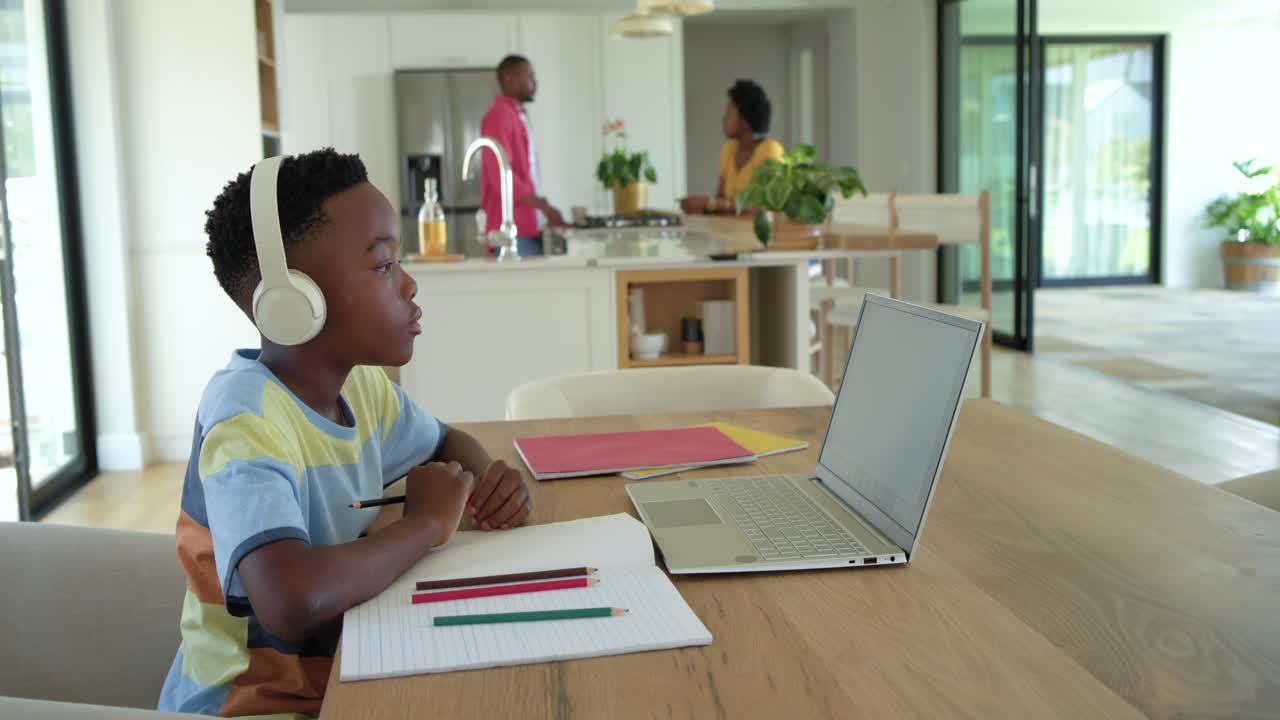 African American child boy at table, responding to laptop for class, writing notebook, copy space