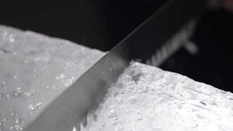a bartender is cutting the ice block to smaller pieces for cocktail service by using a long toothed knife.