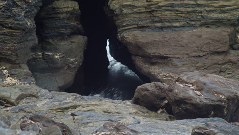 a gap in the rocks with ocean water splashing through a cave in portreath, cornwall