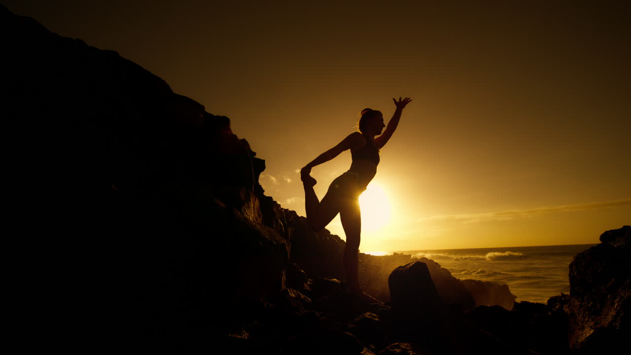 Woman practicing yoga at sunset by the ocean
