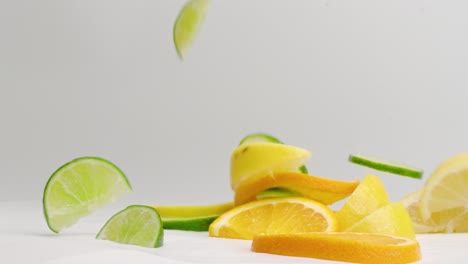 citrus medley of orange, lemon and lime wedges and slices hitting white table in slow motion with juices splattering