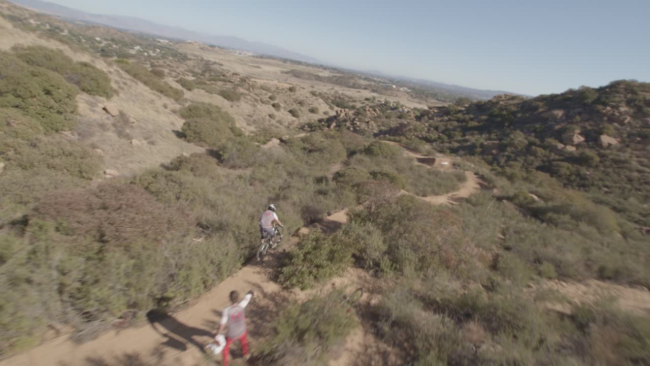 Drone chasing downhill dirt bike rider fast turning and jumping off ramps with tricks