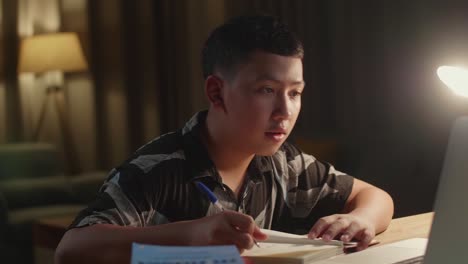 teenage boy learning online from laptop at night