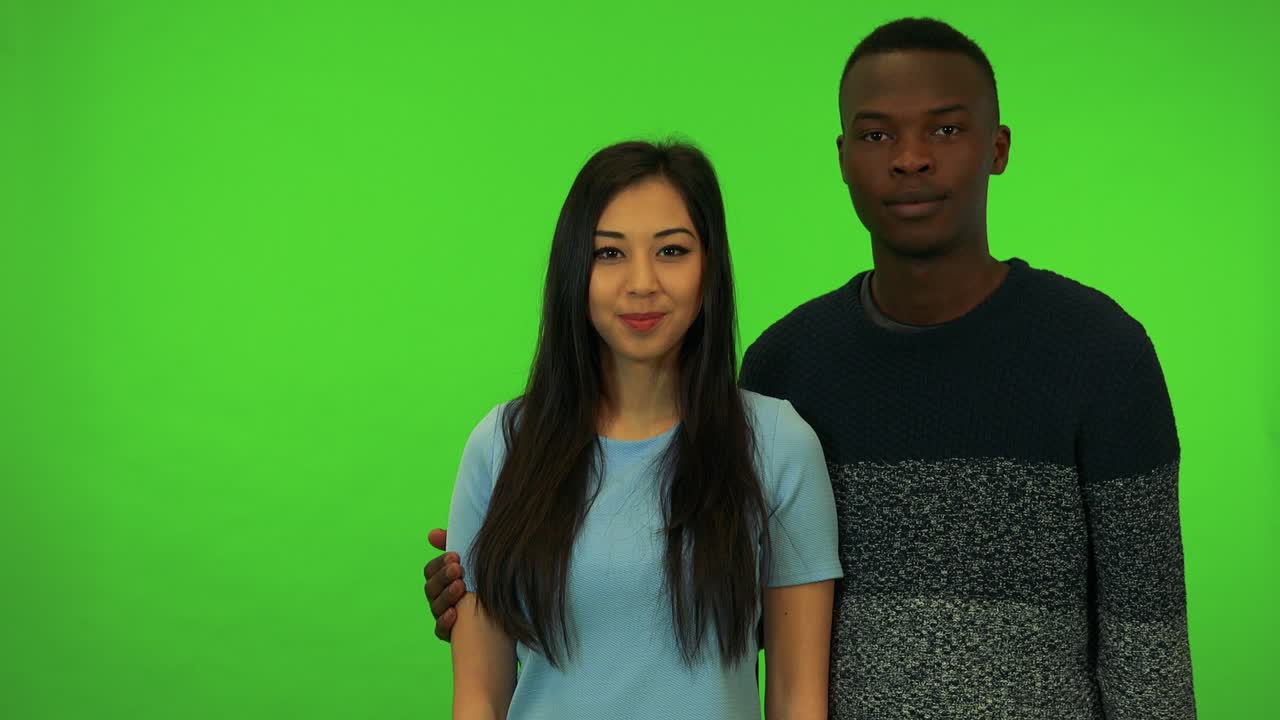 Uma jovem mulher asiática e um jovem homem negro apontam para a câmera e acenam com a cabeça - estúdio de tela verde