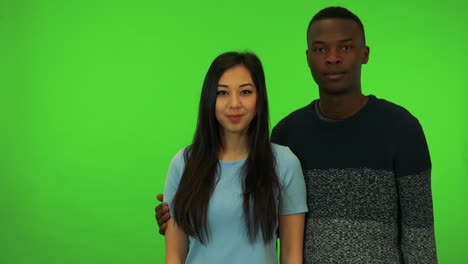 a young asian woman and a young black man point at the camera and nod - green screen studio