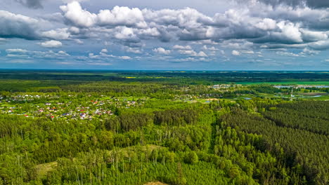 a fast-paced aerial hyper-lapse from a drone flies forward over a vast, vibrant green forest and a picturesque rural village under a dramatic cloudy sky in the latvian countryside