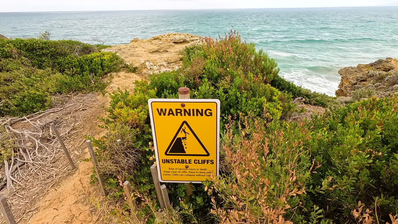 A warning sign near unstable cliffs with ocean view, captured in daylight at Aireys Inlet, Victoria, Australia