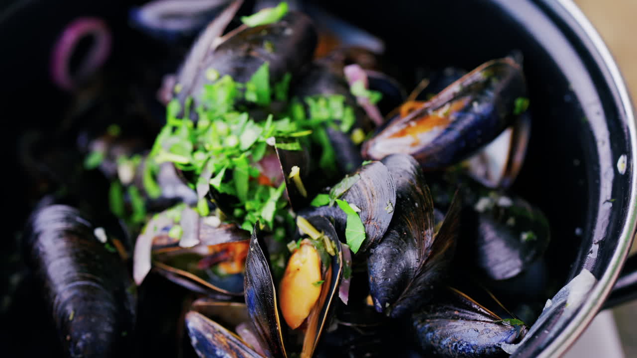 Close up of multiple steamy mussels in a pot with parsley on top