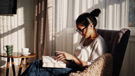 woman relaxing and reading a book in a cozy armchair by a sunny window