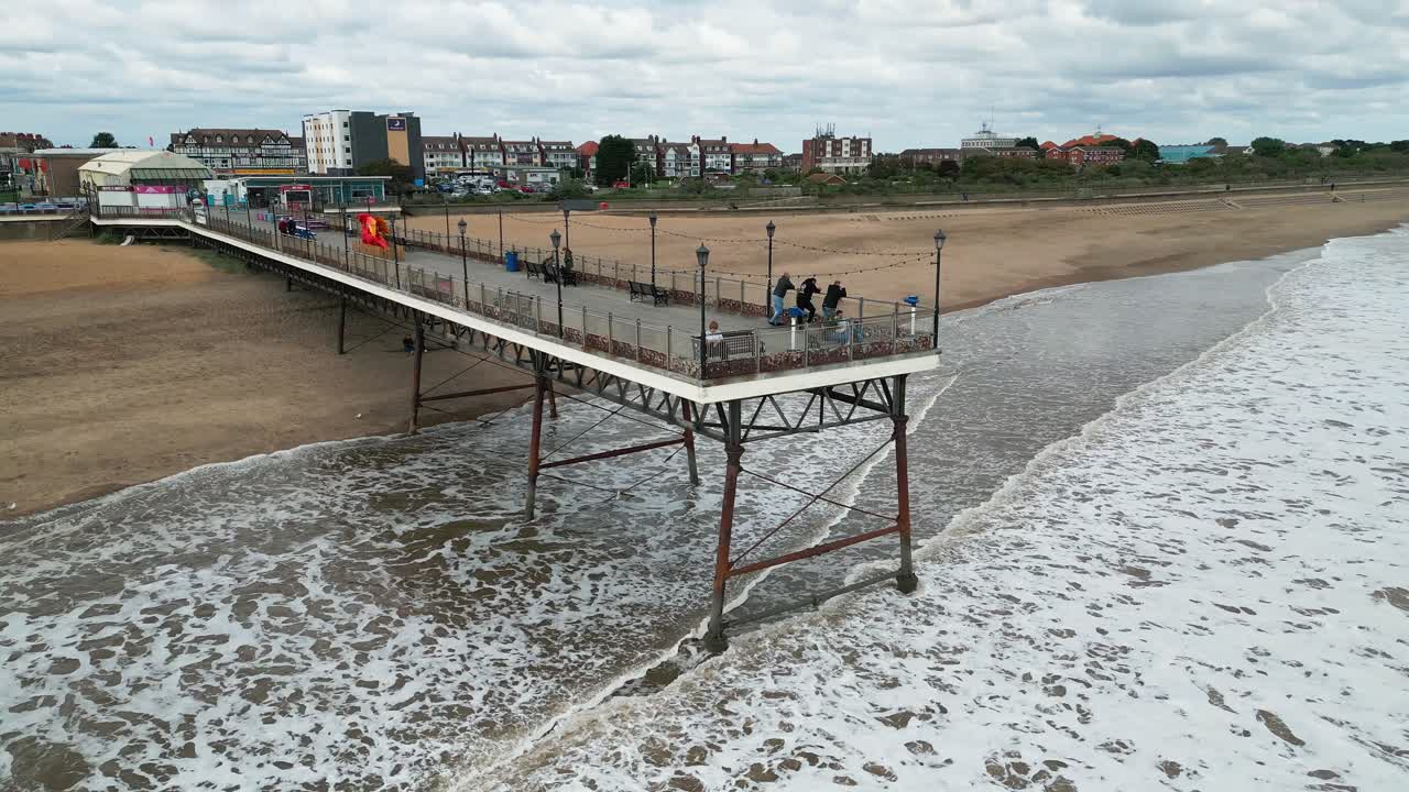 típico balneario inglés, fotografiado con un dron, dando un punto de vista aéreo alto que muestra una amplia extensión de playa de arena con un muelle y olas rompientes-3