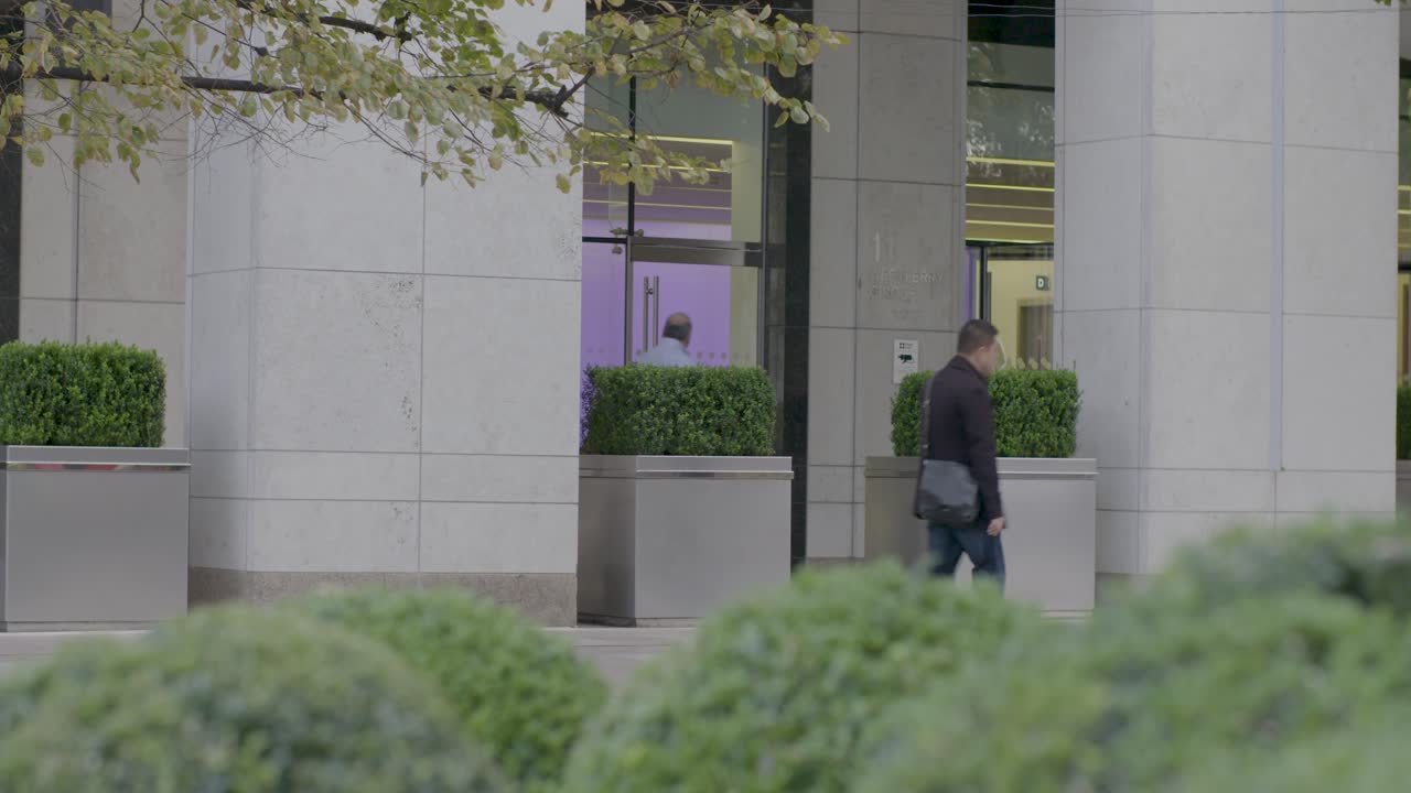 Red city bus passes by modern building with greenery in the foreground