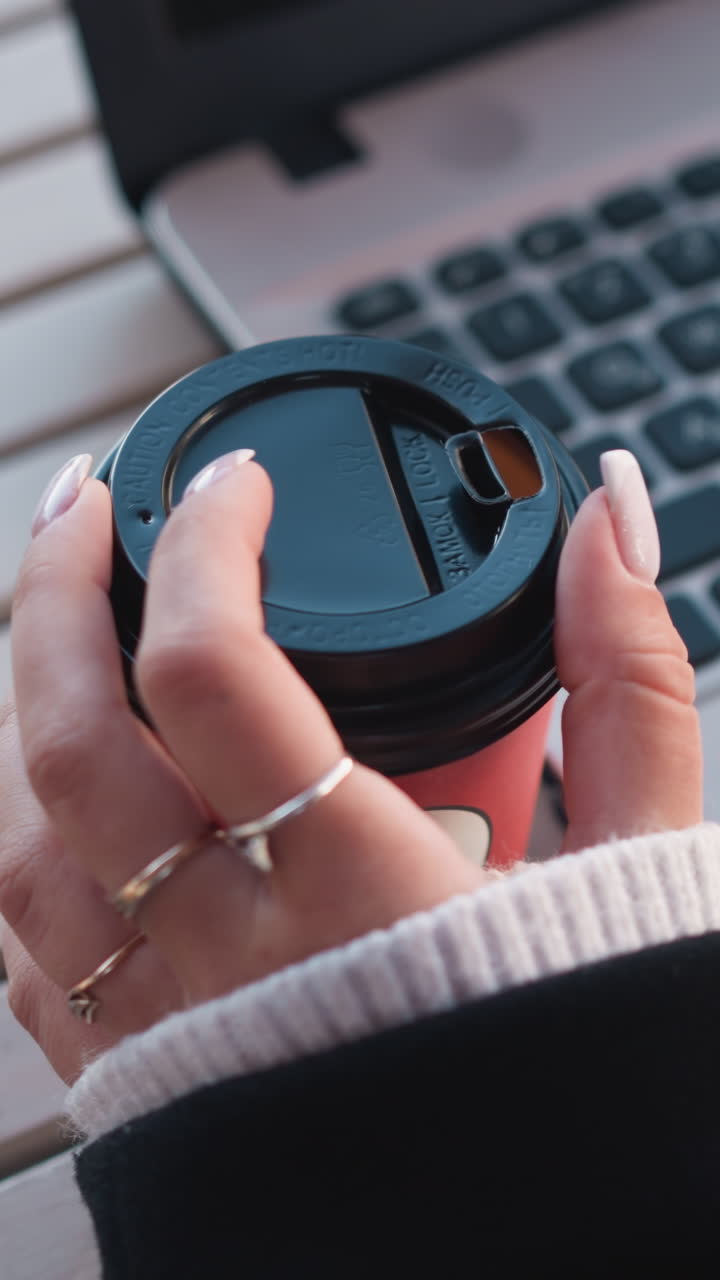 primer plano de la mano de una dama girando suavemente una taza de café cerca de una computadora portátil, destacando sus dedos cuidados contra el teclado de la laptop en un entorno profesional