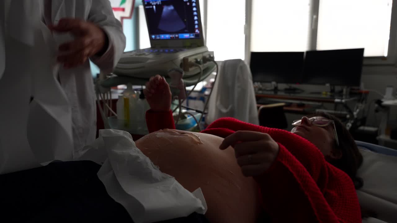 Ginecologo che pulisce con attenzione il gel per ecografia sulla sua paziente incinta.