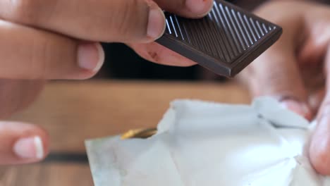 person unwrapping and holding a piece of dark chocolate