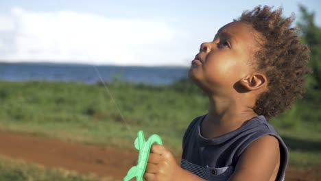 close up shot of a young mixed raced child flying a kite by a lake in africa