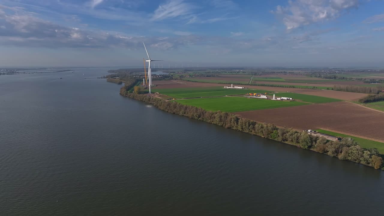 Forward drone flight over Dutch fields showing a distant windmill near water with farmland and a farmhouse.