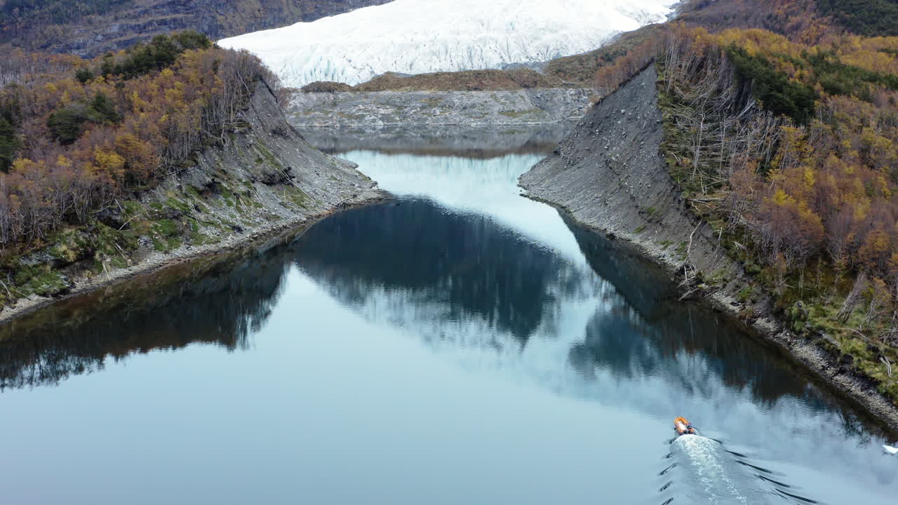 Curved river bends through lush valley with forest and hills in remote Patagonia region as speedboat enters narrows below glacier