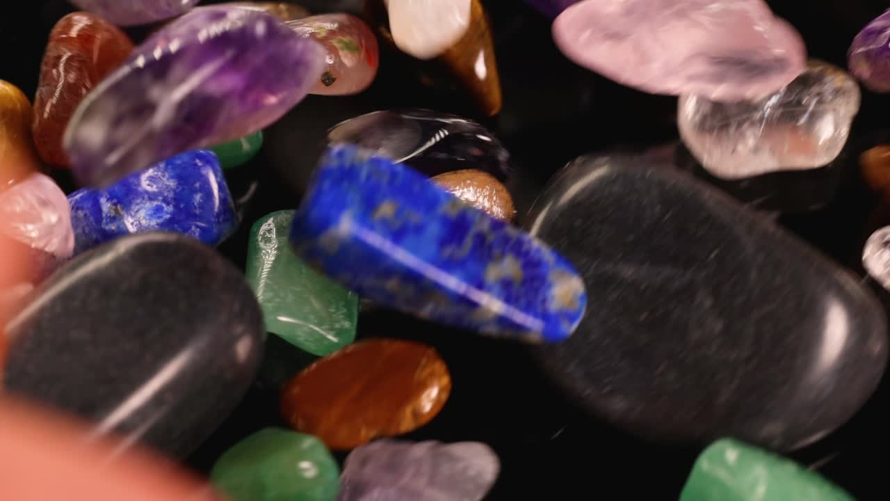 Pedras de chakra vibrantes caem em cascata sobre uma superfície preta, destacando suas cores e texturas sob iluminação suave.