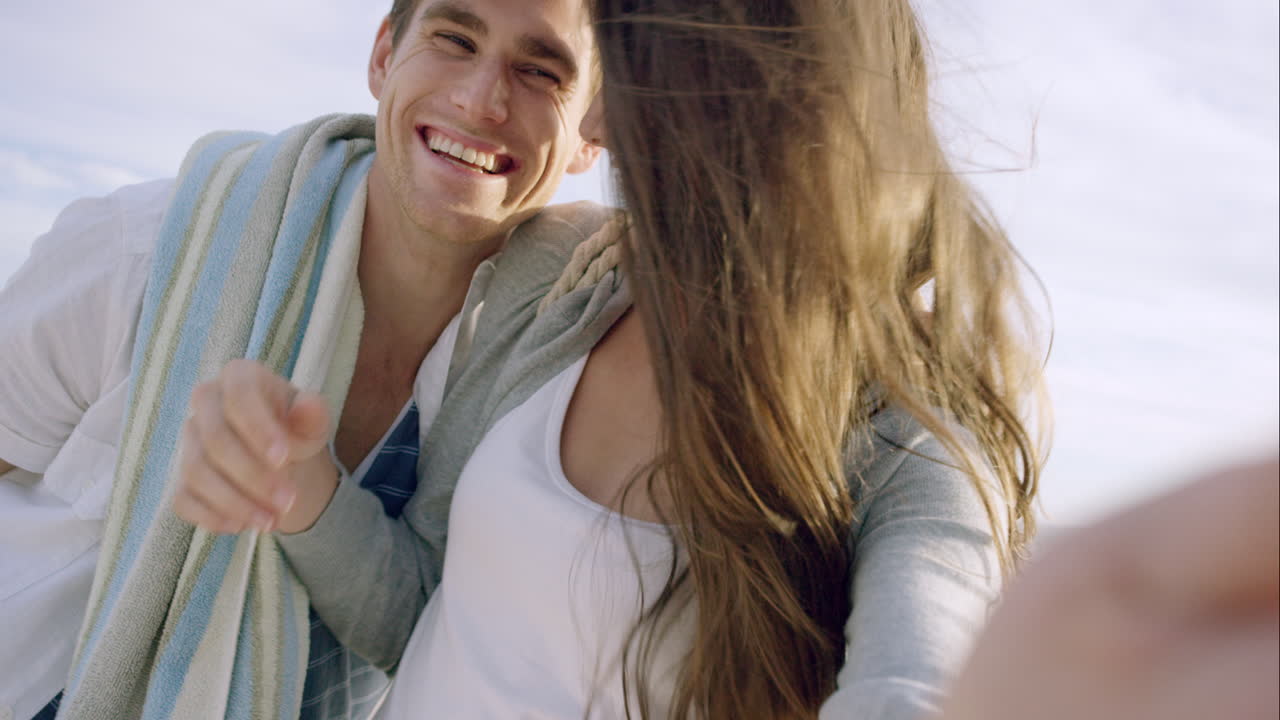 해가 지는 해변에서 셀카를 찍는 행복한 커플. 휴가 중 자연과 라이프 스타일을 즐기며 미소 짓고 회전하는 전화기를 사용합니다.