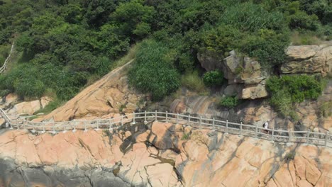 zoom out aerial reveal shot of man with backpack walking along rocky coastal trail