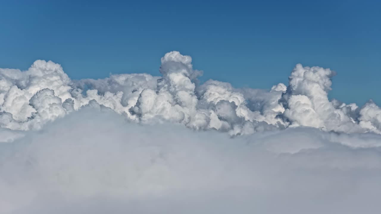 Telephoto aerial tracking shot gliding above clouds under calm blue sky