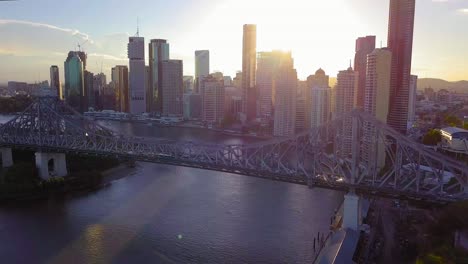 Forward-moving-aerial-view-of-a-city-center-with-tall-buildings-and-bridge-over-the-river-at-sunset
