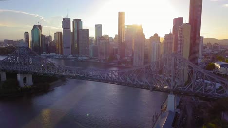 forward moving aerial view of a city center with tall buildings and bridge over the river at sunset