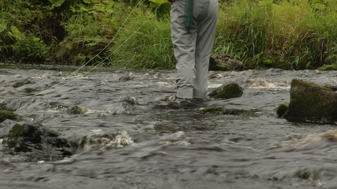 Tilting shot of a fly fisherman casting his line into a peaceful pool with a river