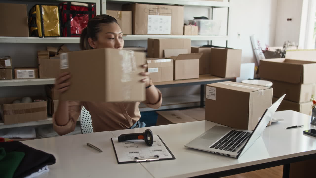 Female Manager Scanning Parcels at Desk with Laptop at Storage Office