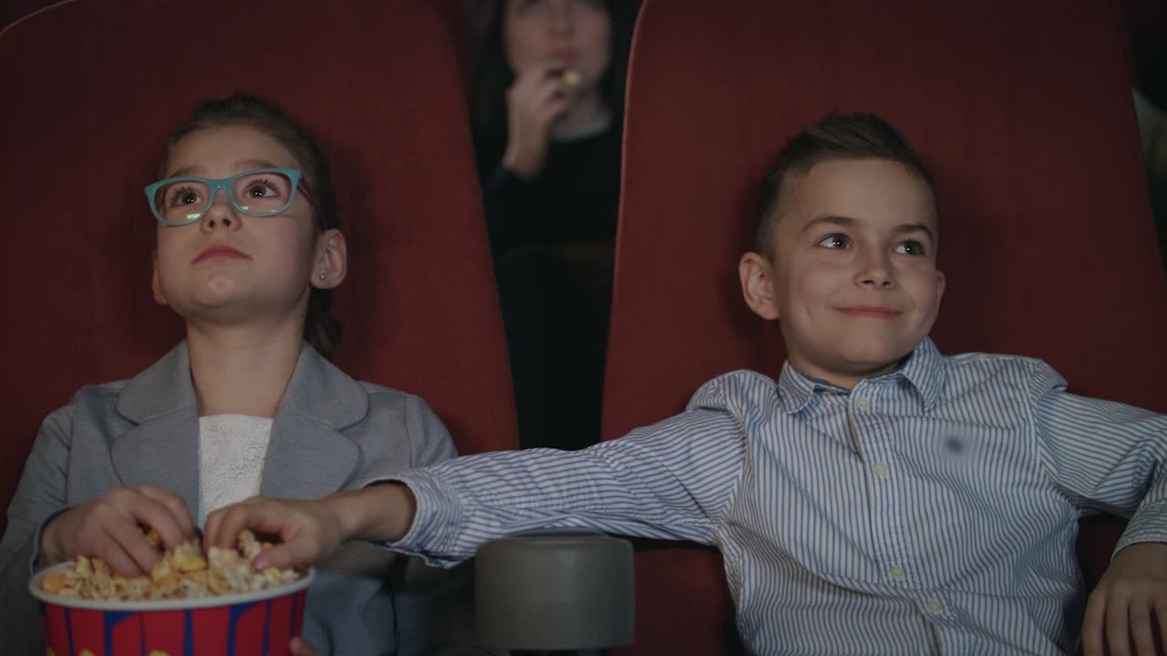 los niños comen palomitas de maíz en el cine. los niños en edad preescolar ven películas en el cine.