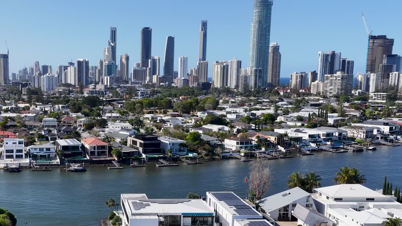 Drone pans across canal homes and high-rise skyline under bright daylight, Gold Coast, Australia