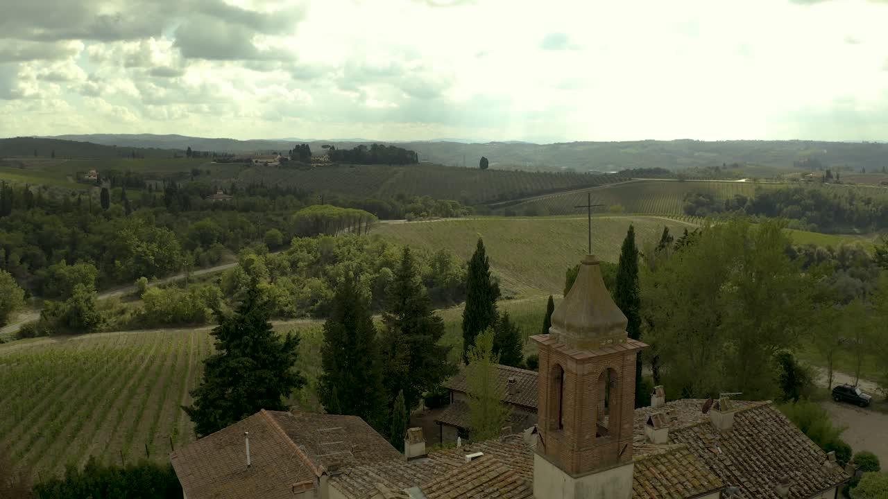 lento y dramático sobrevuelo aéreo cerca de la cruz en la parte superior del campanario exterior de la antigua iglesia, con viñedos y colinas circundantes en la toscana, italia