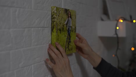 side view happy young woman putting picture or photo in frame on fireplace, decorating living room. smiling female homeowner enjoying improving interior, making apartment cozy. moving concept.