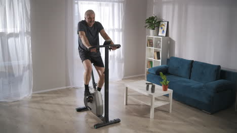 moderna bicicleta estacionaria para el entrenamiento en el hogar hombre de mediana edad lo está usando para mantenerse en forma y salud ejercicios de cardio