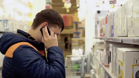 Young-guy-is-talking-on-the-phone-standing-in-electrical-goods-department-chandeliers-in-the-building-materials-store