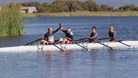 Four-senior-caucasian-men-and-women-in-rowing-boat-high-fiving