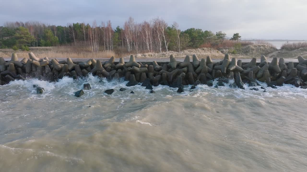 Aerial establishing view of Port of Liepaja concrete pier, Baltic sea coastline day, big waves splashing, slow motion drone shot moving backward