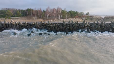 vista aérea del muelle de hormigón del puerto de liepaja, día de la costa del mar báltico, grandes olas salpicando, tiro de drones en cámara lenta moviéndose hacia atrás