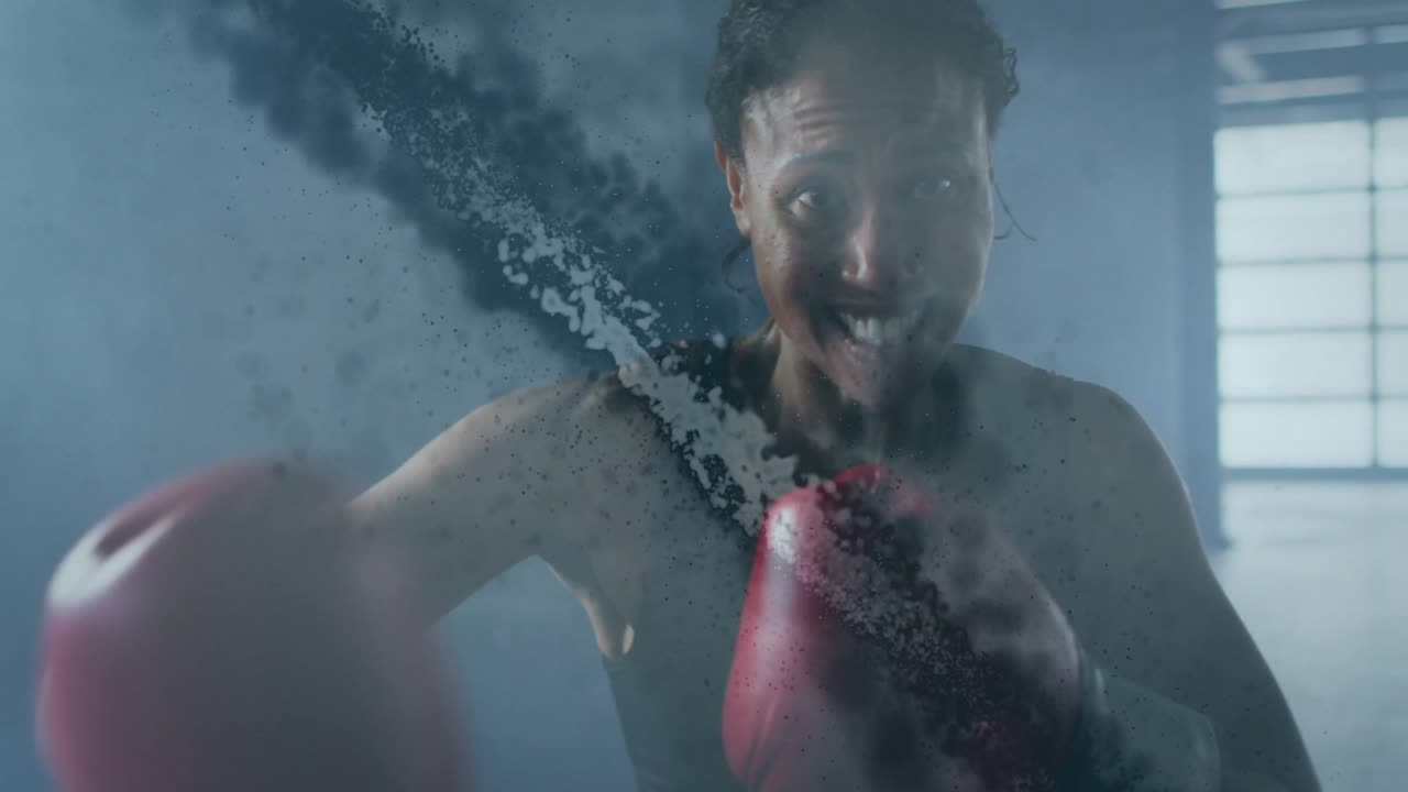 Female boxer training gym, raising red gloves moving in and punching at camera through dust cloud