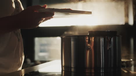 a woman cooks soup on an electric stove. putting the chopped vegetables into the pot