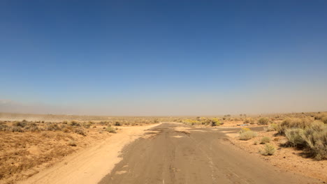 driving down a desolate mojave desert road covered with sand by wind and storms - point of view