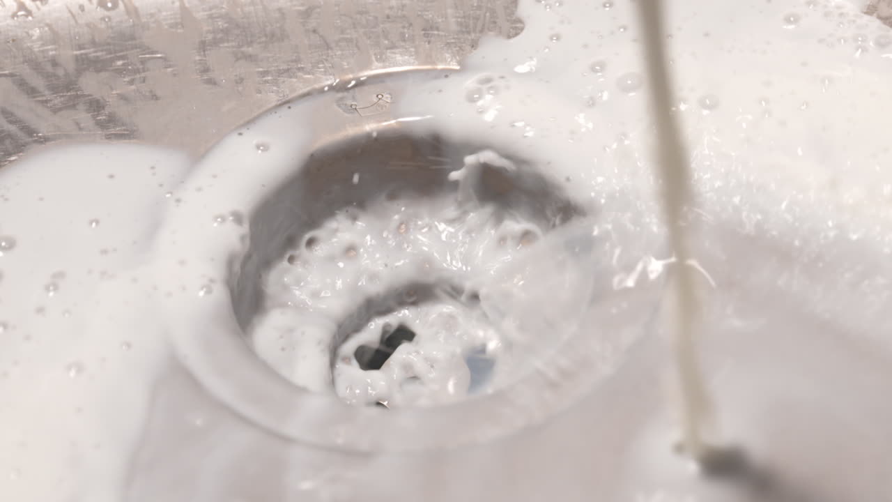 우유가 부엌 싱크대에 쏟아져 배수구로 흘러내립니다.
