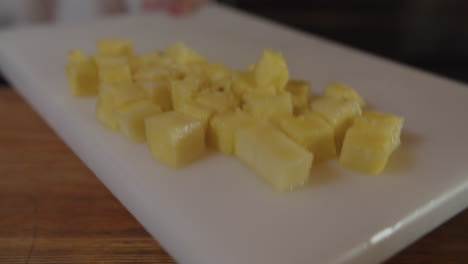 hermosa foto en cámara lenta de una camarera levantando una tabla de cortar blanca con muchos pedazos pequeños de piña cortados en ella para poner en una licuadora para preparar un cóctel